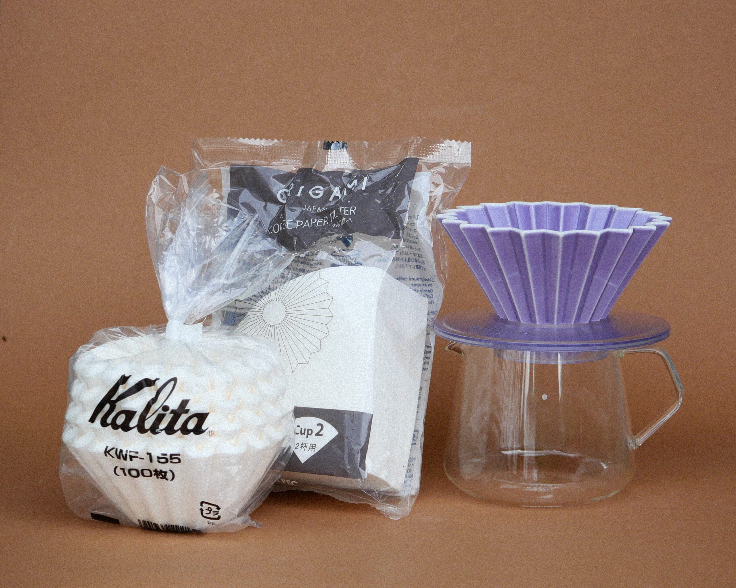 Kaffee Glaskanne mit Origami Filterhalter in purple, links davon Origami und Kalita Wave Filterpapier