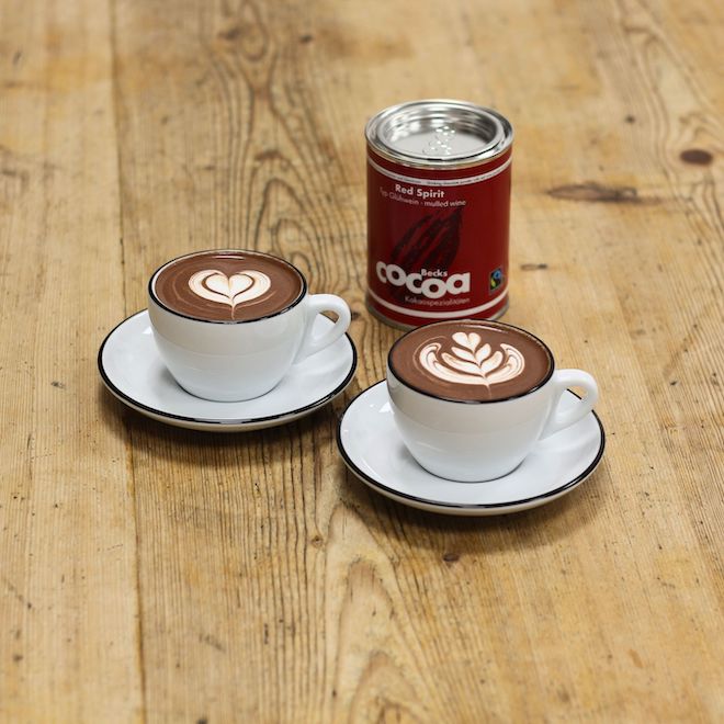 Glühkakao Trinkschokolade in Dose und zwei Tassen mit Glühkakao gefüllt und Latte Art verziert