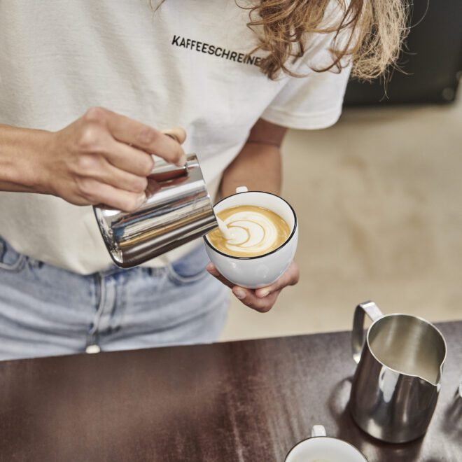 Kaffeeschreinerin Lara giesst Latte Art Tulip für den Cappuccino