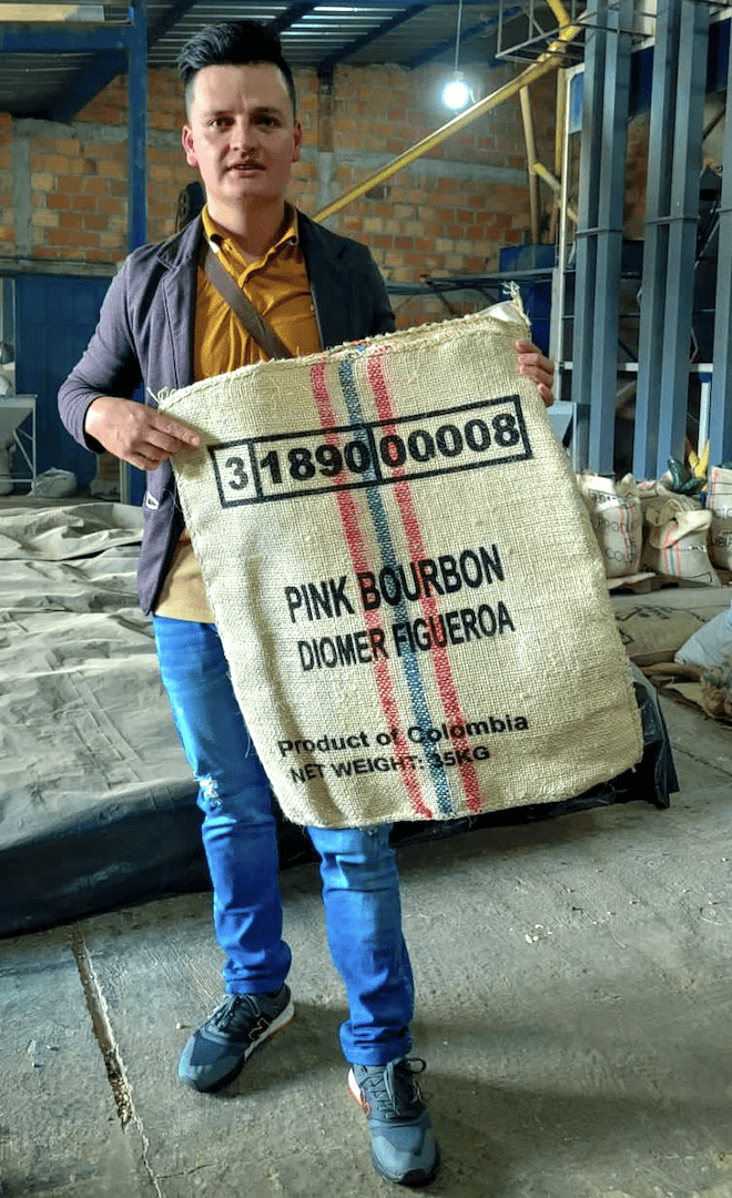 Diomer Figueroa in der Dry Mill in Kolumbien, Huila, mit Kaffeesack in den Händen, der mit seinen Daten beschriftet ist